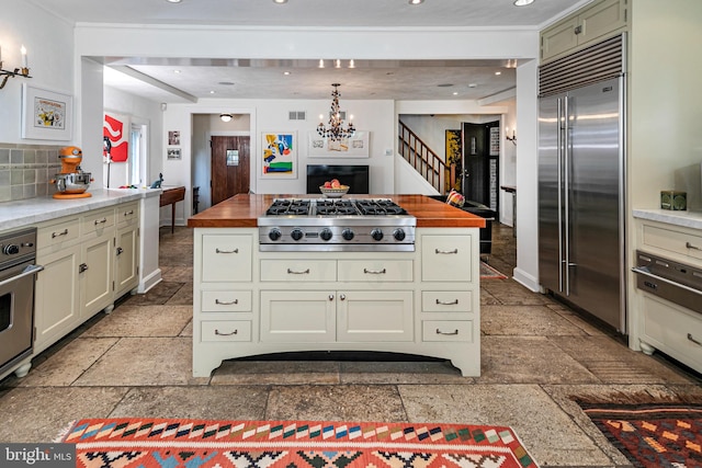 kitchen with appliances with stainless steel finishes, hanging light fixtures, tasteful backsplash, and wooden counters