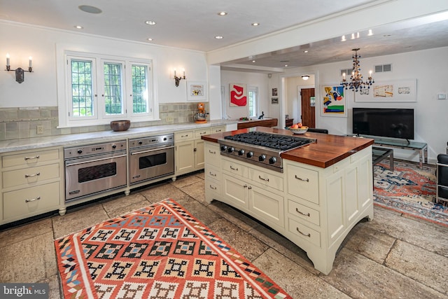 kitchen with an inviting chandelier, a kitchen island, stainless steel appliances, backsplash, and butcher block countertops