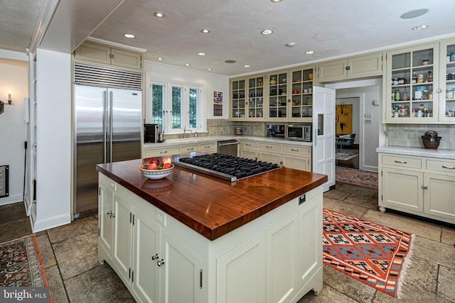 kitchen with sink, butcher block countertops, stainless steel appliances, a center island, and decorative backsplash