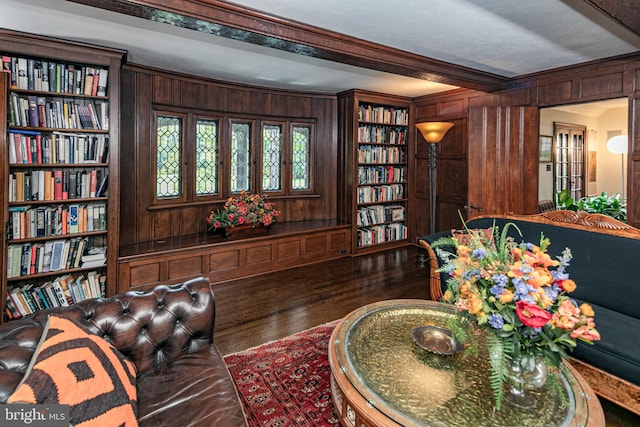 living area with dark wood-type flooring, wood walls, crown molding, and built in shelves