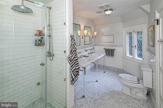 bathroom with double sink, tile walls, a shower with shower door, and toilet