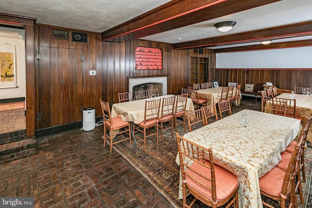 dining area featuring wooden walls, beamed ceiling, and a textured ceiling