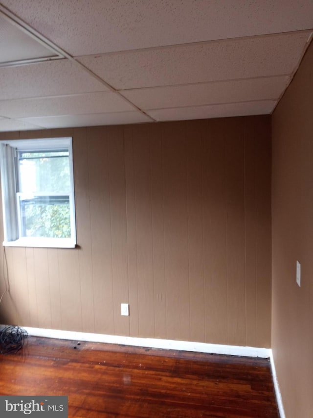 unfurnished room featuring a drop ceiling, wood walls, and dark hardwood / wood-style floors