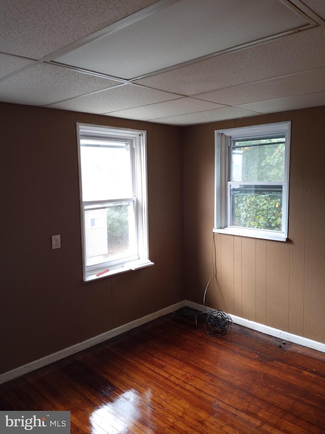 empty room featuring a healthy amount of sunlight, dark hardwood / wood-style floors, and a paneled ceiling