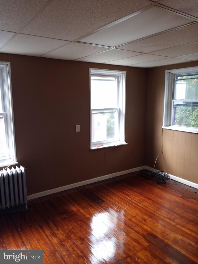 empty room with radiator heating unit, dark hardwood / wood-style floors, plenty of natural light, and a paneled ceiling