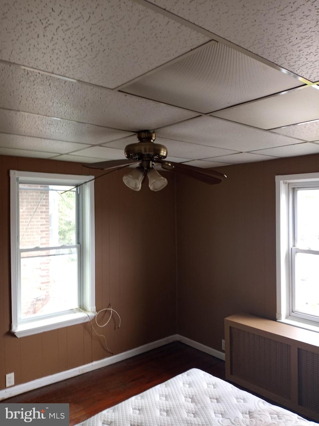 unfurnished bedroom featuring radiator heating unit, ceiling fan, multiple windows, and a paneled ceiling