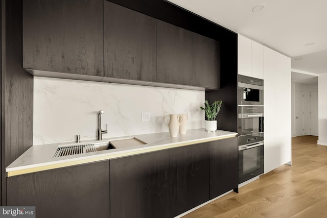 kitchen featuring light hardwood / wood-style floors, tasteful backsplash, white cabinets, sink, and double oven