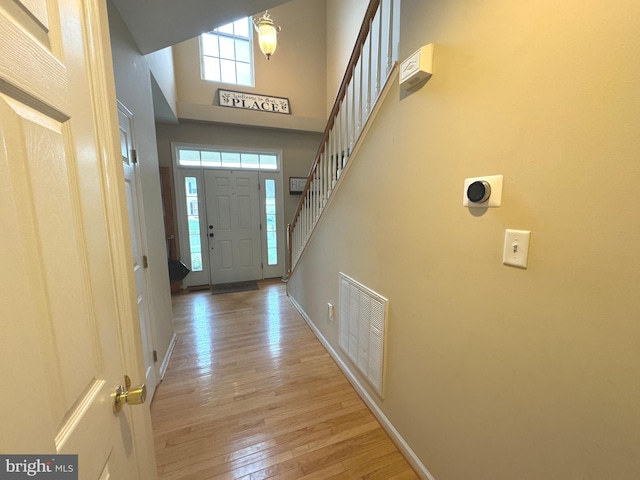 foyer entrance with a towering ceiling, light wood-style flooring, visible vents, and baseboards