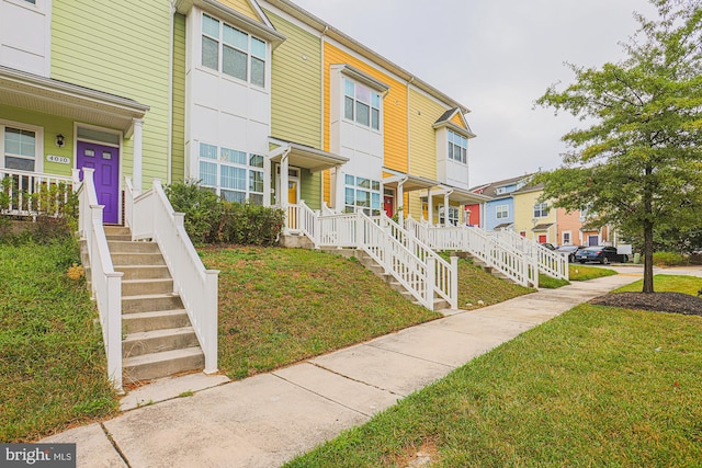 townhome / multi-family property featuring covered porch and a front yard