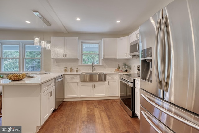 kitchen with sink, white cabinetry, light hardwood / wood-style floors, stainless steel appliances, and pendant lighting