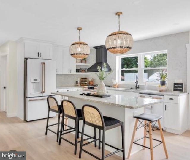 kitchen with hanging light fixtures, white cabinets, white appliances, a kitchen island, and wall chimney range hood