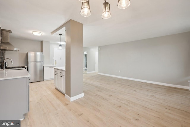 kitchen featuring white cabinets, stove, stainless steel fridge, decorative light fixtures, and light hardwood / wood-style flooring