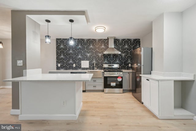 kitchen featuring light wood-type flooring, wall chimney range hood, backsplash, appliances with stainless steel finishes, and decorative light fixtures