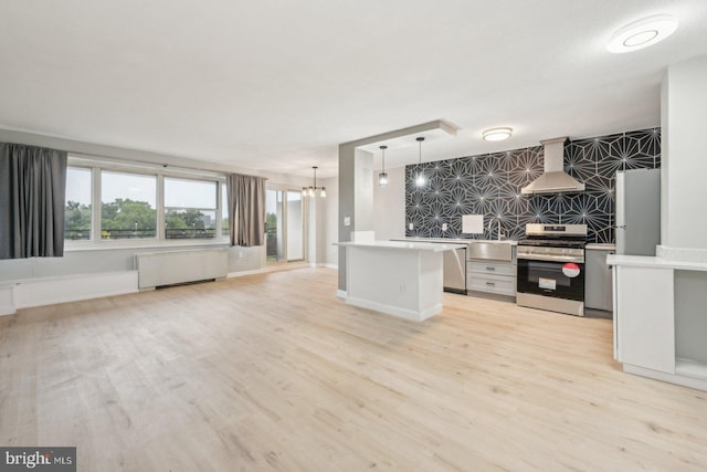 kitchen with light hardwood / wood-style floors, wall chimney exhaust hood, pendant lighting, radiator heating unit, and stainless steel appliances