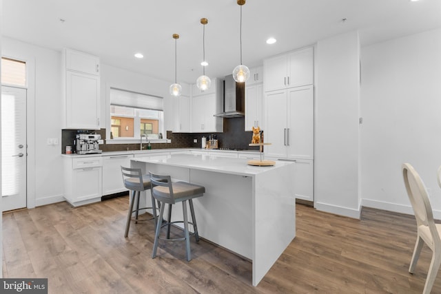 kitchen featuring a kitchen island, wall chimney range hood, dishwasher, and white cabinets