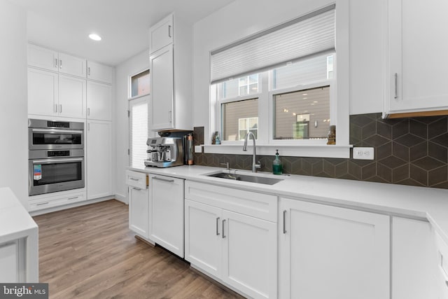 kitchen with sink, tasteful backsplash, wood-type flooring, white cabinetry, and stainless steel double oven