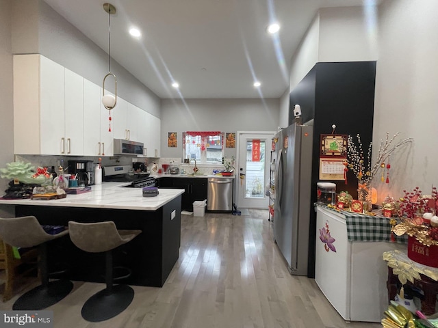 kitchen featuring light wood-type flooring, white cabinetry, kitchen peninsula, stainless steel appliances, and decorative light fixtures