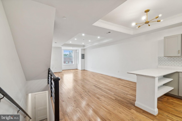 unfurnished living room with a notable chandelier, a tray ceiling, light wood-type flooring, and ornamental molding