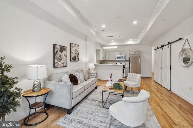 living room featuring a tray ceiling, light hardwood / wood-style floors, crown molding, and a barn door