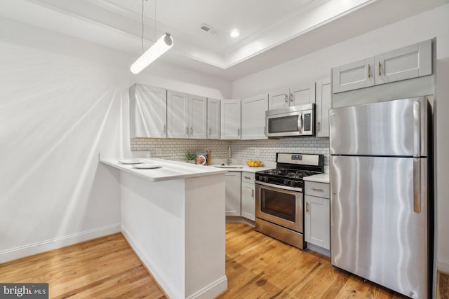 kitchen featuring light hardwood / wood-style floors, kitchen peninsula, hanging light fixtures, backsplash, and appliances with stainless steel finishes