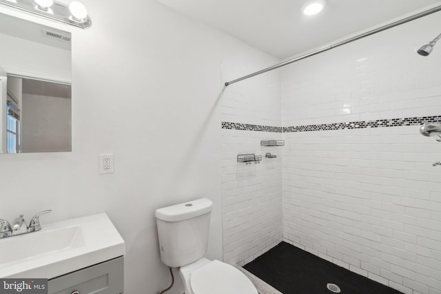 bathroom featuring a tile shower, vanity, and toilet