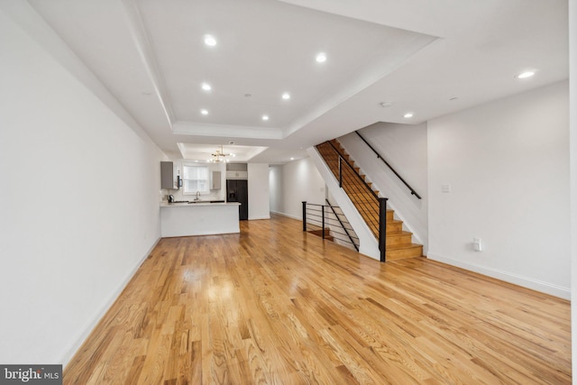 unfurnished living room with light wood-type flooring, a chandelier, and a raised ceiling