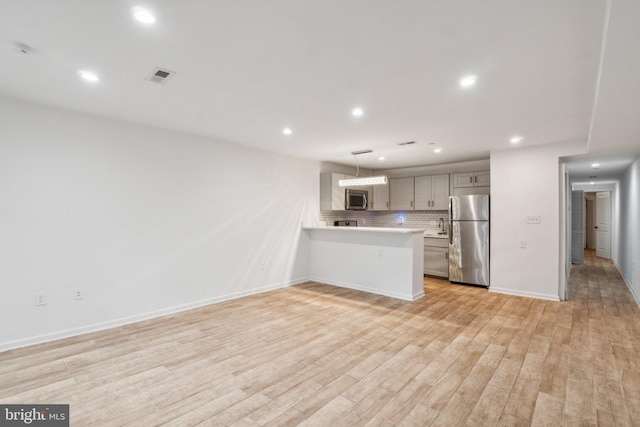 kitchen featuring light hardwood / wood-style floors, kitchen peninsula, hanging light fixtures, backsplash, and appliances with stainless steel finishes