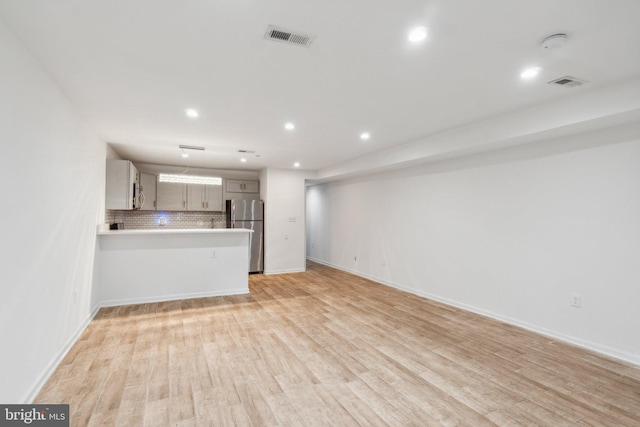 kitchen featuring light wood-type flooring, kitchen peninsula, stainless steel appliances, backsplash, and light brown cabinetry