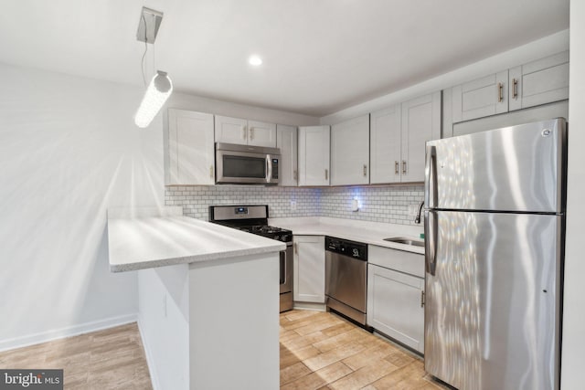 kitchen with stainless steel appliances, kitchen peninsula, hanging light fixtures, and light wood-type flooring