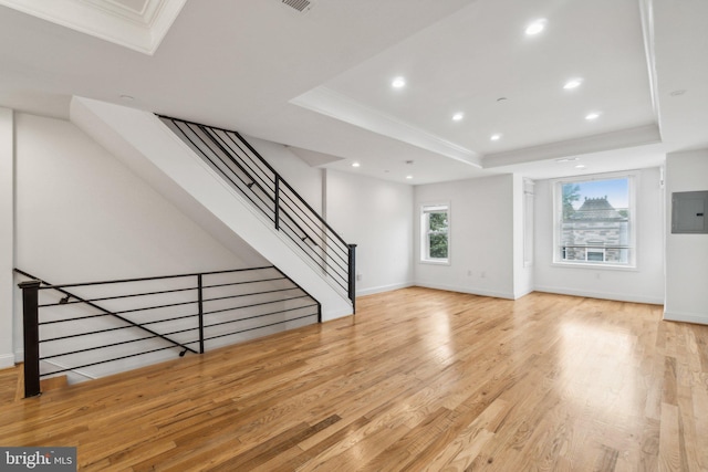 unfurnished living room featuring ornamental molding, light wood-type flooring, a raised ceiling, and electric panel