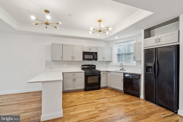 kitchen featuring black appliances, kitchen peninsula, a tray ceiling, and a chandelier