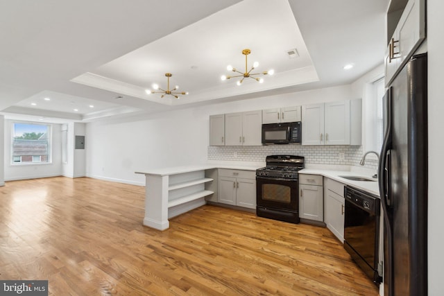 kitchen with a notable chandelier, a tray ceiling, kitchen peninsula, and black appliances