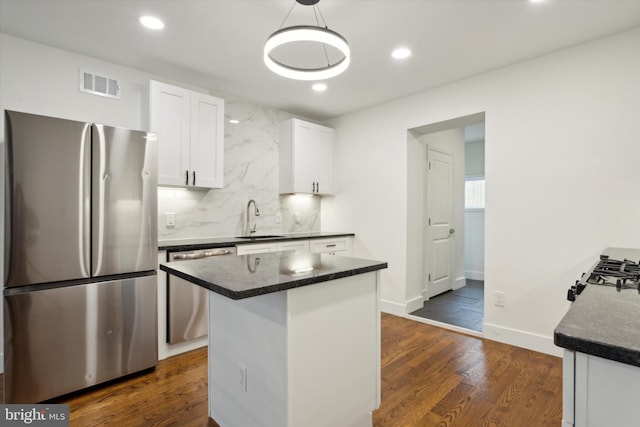 kitchen with appliances with stainless steel finishes, hanging light fixtures, dark wood-type flooring, white cabinets, and sink