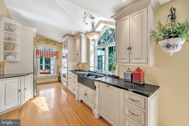 kitchen featuring pendant lighting, light wood-type flooring, vaulted ceiling, and stainless steel appliances