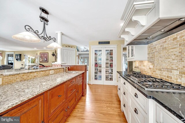 kitchen featuring white cabinetry, stainless steel gas cooktop, light wood-type flooring, decorative light fixtures, and sink