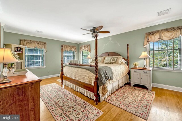 bedroom featuring multiple windows, light hardwood / wood-style floors, ornamental molding, and ceiling fan