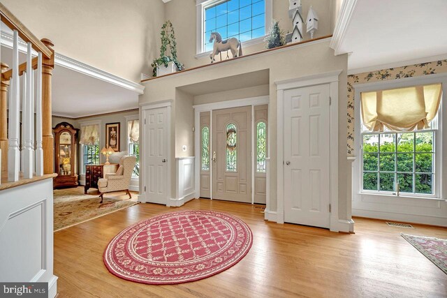 entrance foyer featuring light hardwood / wood-style flooring, a towering ceiling, and ornamental molding