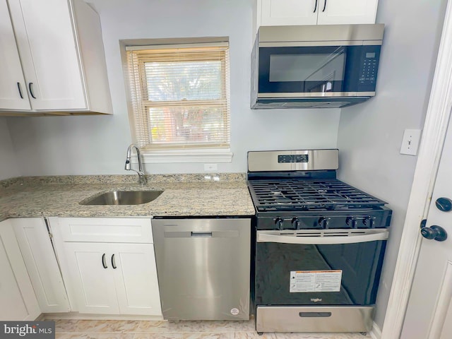 kitchen with light stone counters, white cabinets, appliances with stainless steel finishes, and sink