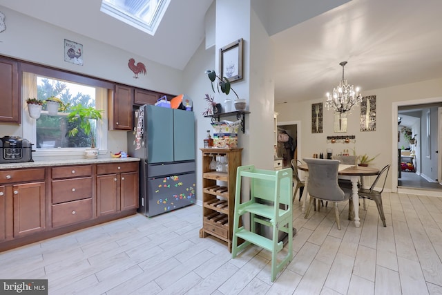 kitchen featuring stainless steel fridge, pendant lighting, vaulted ceiling with skylight, an inviting chandelier, and light hardwood / wood-style flooring