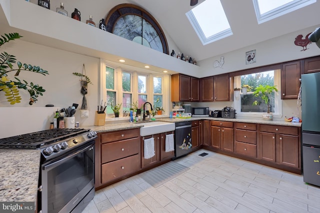 kitchen with light stone counters, high vaulted ceiling, stainless steel appliances, a skylight, and sink