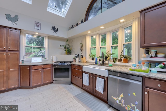 kitchen with a skylight, sink, high vaulted ceiling, stainless steel appliances, and light stone countertops