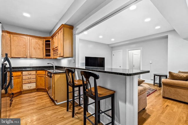 kitchen featuring dark stone counters, kitchen peninsula, light hardwood / wood-style flooring, and a breakfast bar