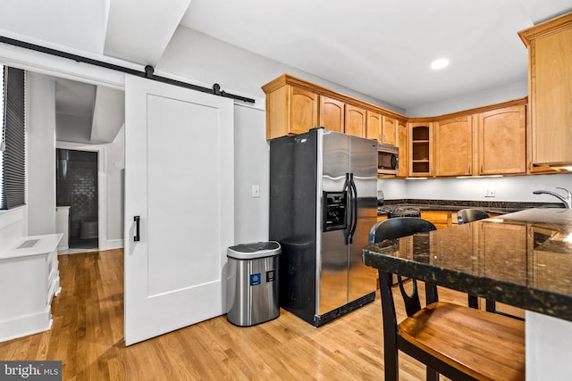 kitchen with dark stone countertops, a barn door, stainless steel appliances, light hardwood / wood-style flooring, and sink