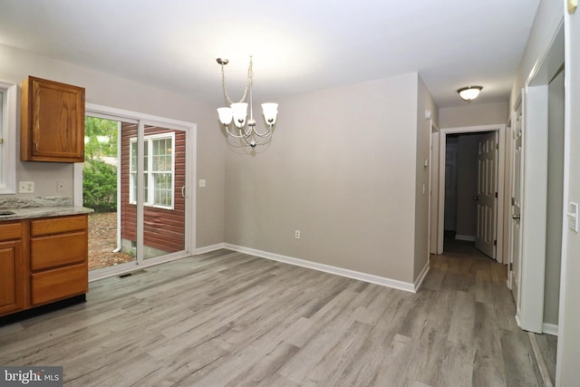 unfurnished dining area featuring an inviting chandelier and light hardwood / wood-style floors