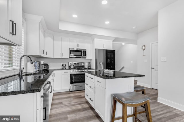 kitchen featuring light wood finished floors, a breakfast bar area, stainless steel appliances, white cabinets, and a sink