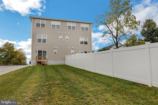 rear view of house featuring entry steps, fence, and a lawn