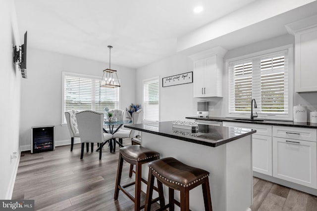 kitchen with dark countertops, a sink, light wood finished floors, and a kitchen bar