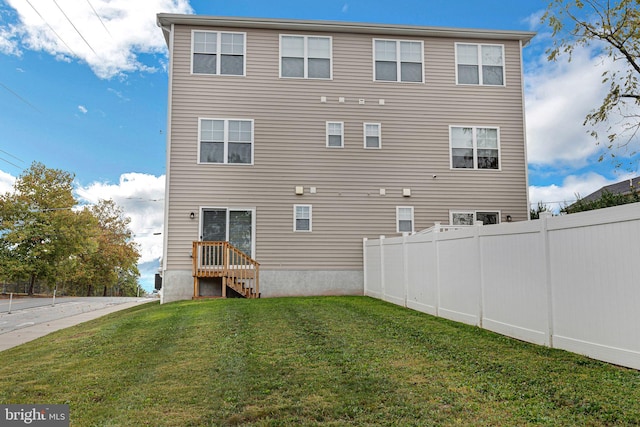 rear view of property featuring a lawn and fence