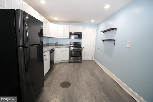 kitchen featuring sink, wood-type flooring, white cabinetry, black appliances, and light stone countertops