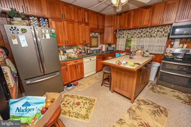 kitchen featuring appliances with stainless steel finishes, a ceiling fan, brown cabinetry, and a center island